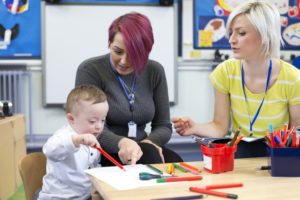 A picture of a consultant sitting beside an educator while she plays with a child painting.