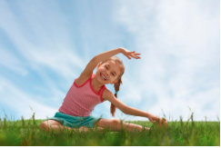 A child in the middle of the field stretching and smiling